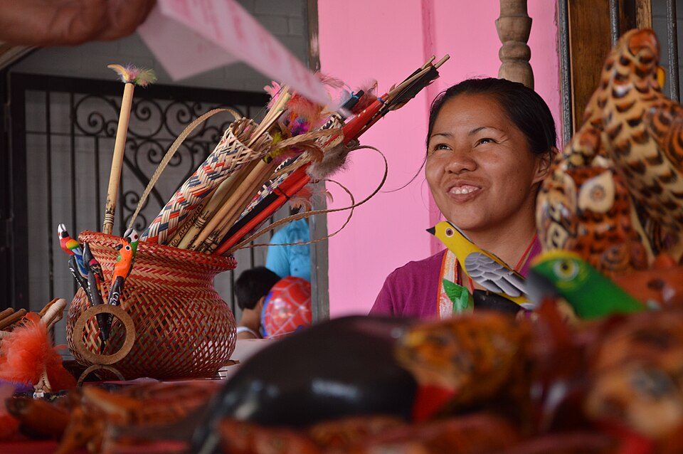 Artesana venezolana sonriente en Tintorero, rodeada de piezas talladas en madera y artesanía tradicional.